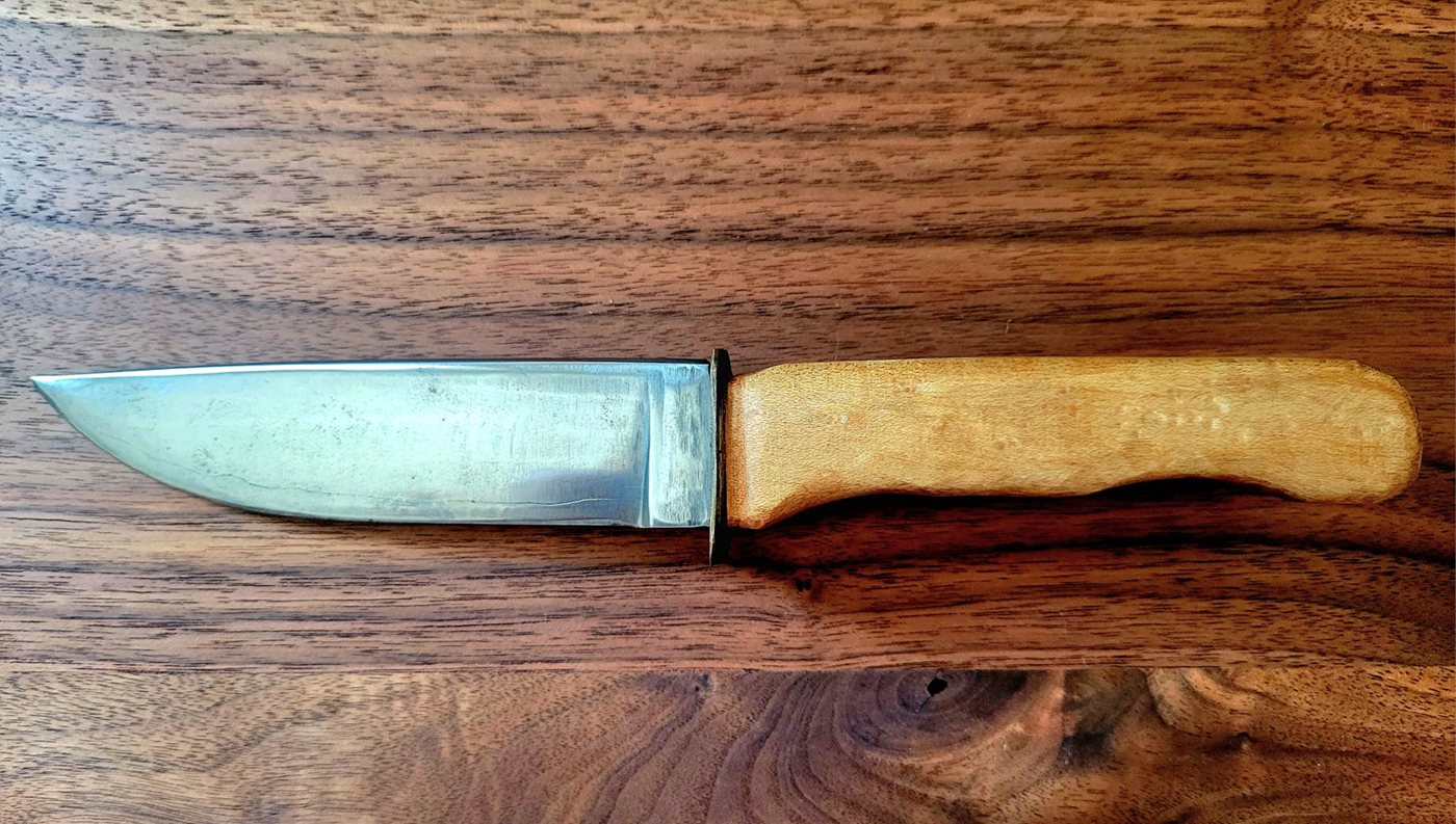 A hand-forged knife with a handmade wooden handle resting on a work surface